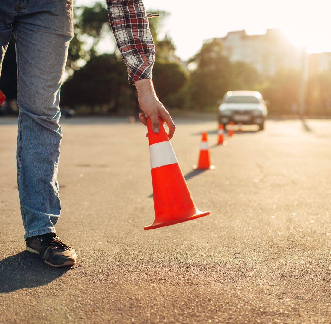 Eine Person hält einen Verkehrshütchen und steht vor einem Auto.