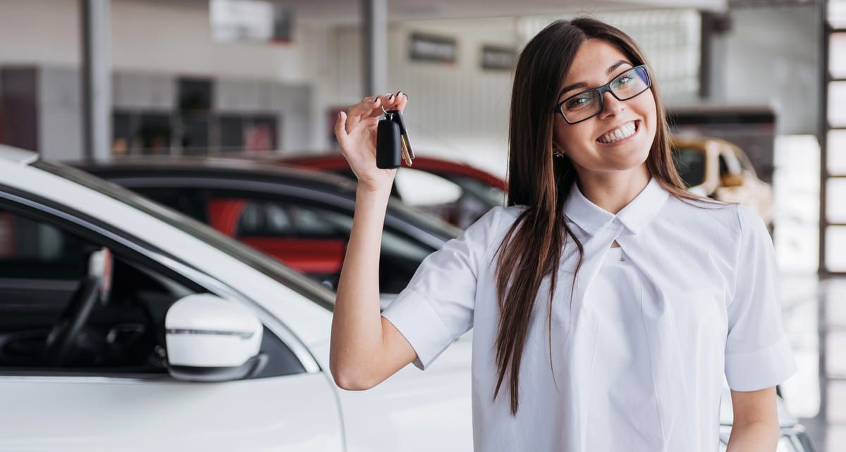 Eine Frau hält einen Autoschlüssel vor einem Auto in der Hand.